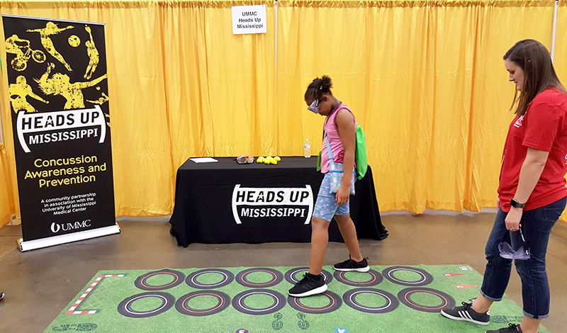 Pediatric nurse practitioner student Christina Shields watches as a Fitness Fest attendee learns more about injuries by trying a physical challenge while wearing concussion goggles.